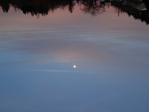 A nearly full moon rises in the last pink rays of sunset